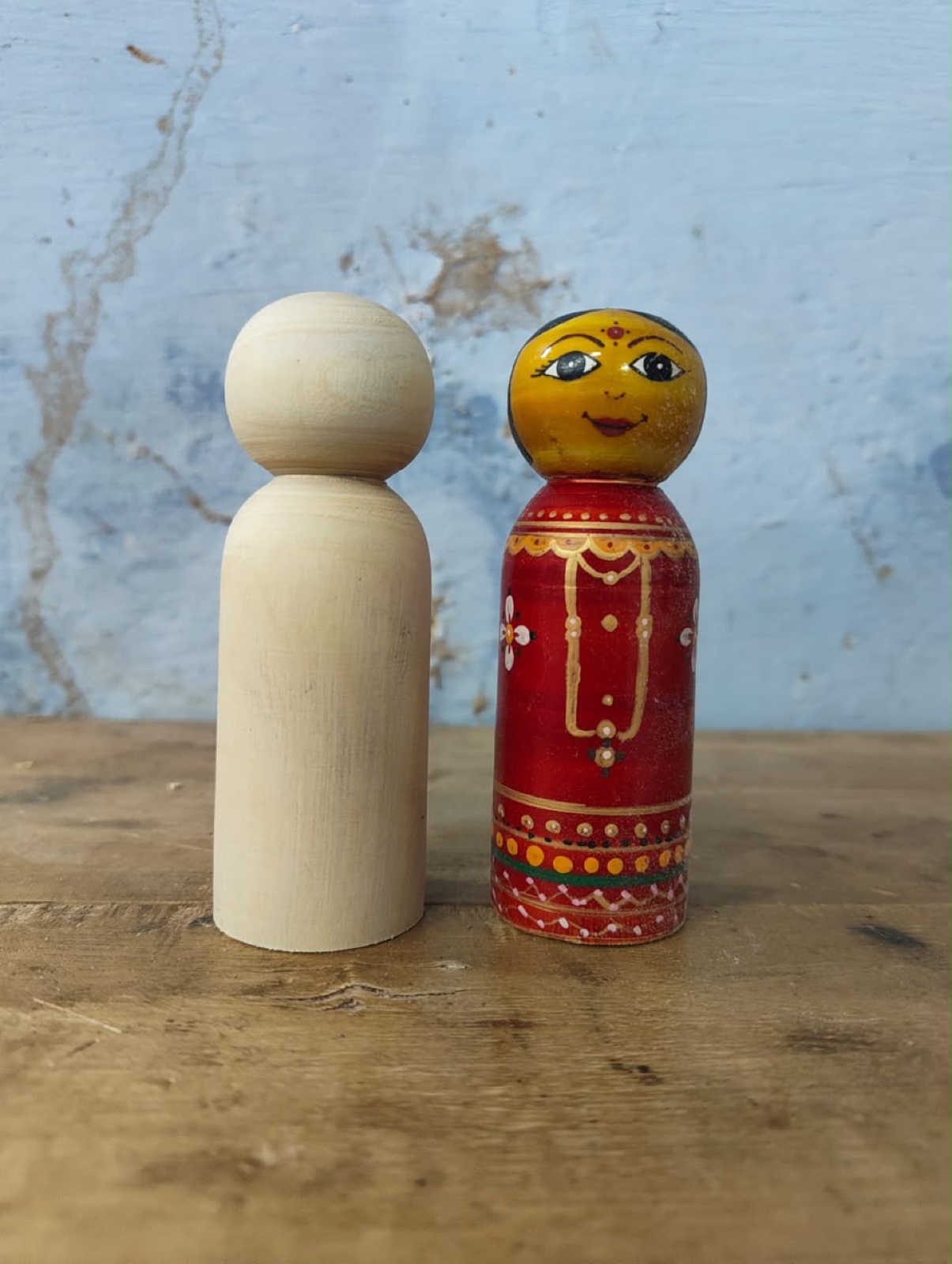 An unfinished turned wooden doll beside a completed hand-painted doll